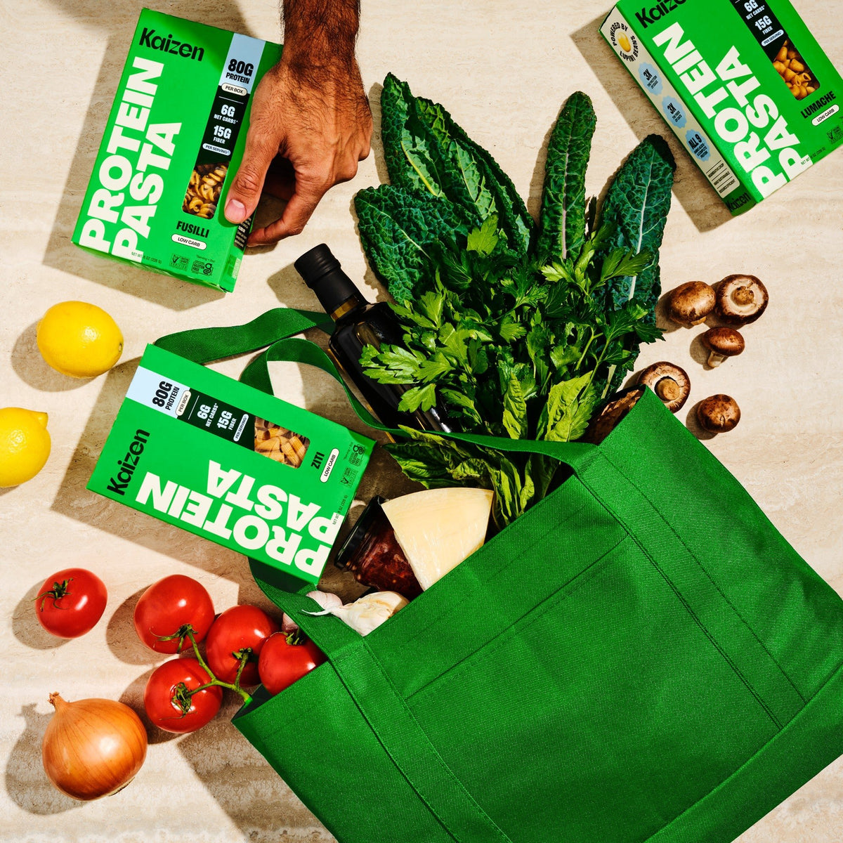 Kaizen Protein Pasta boxes in a green shopping bag with fresh vegetables
