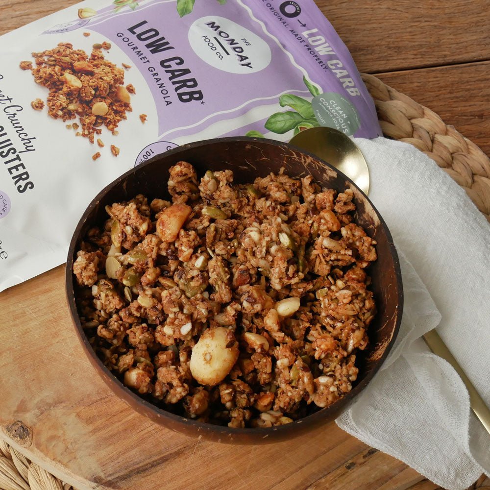 The Monday Food Co macadamia clusters granola in a coconut bowl with a spoon, new-design bag behind