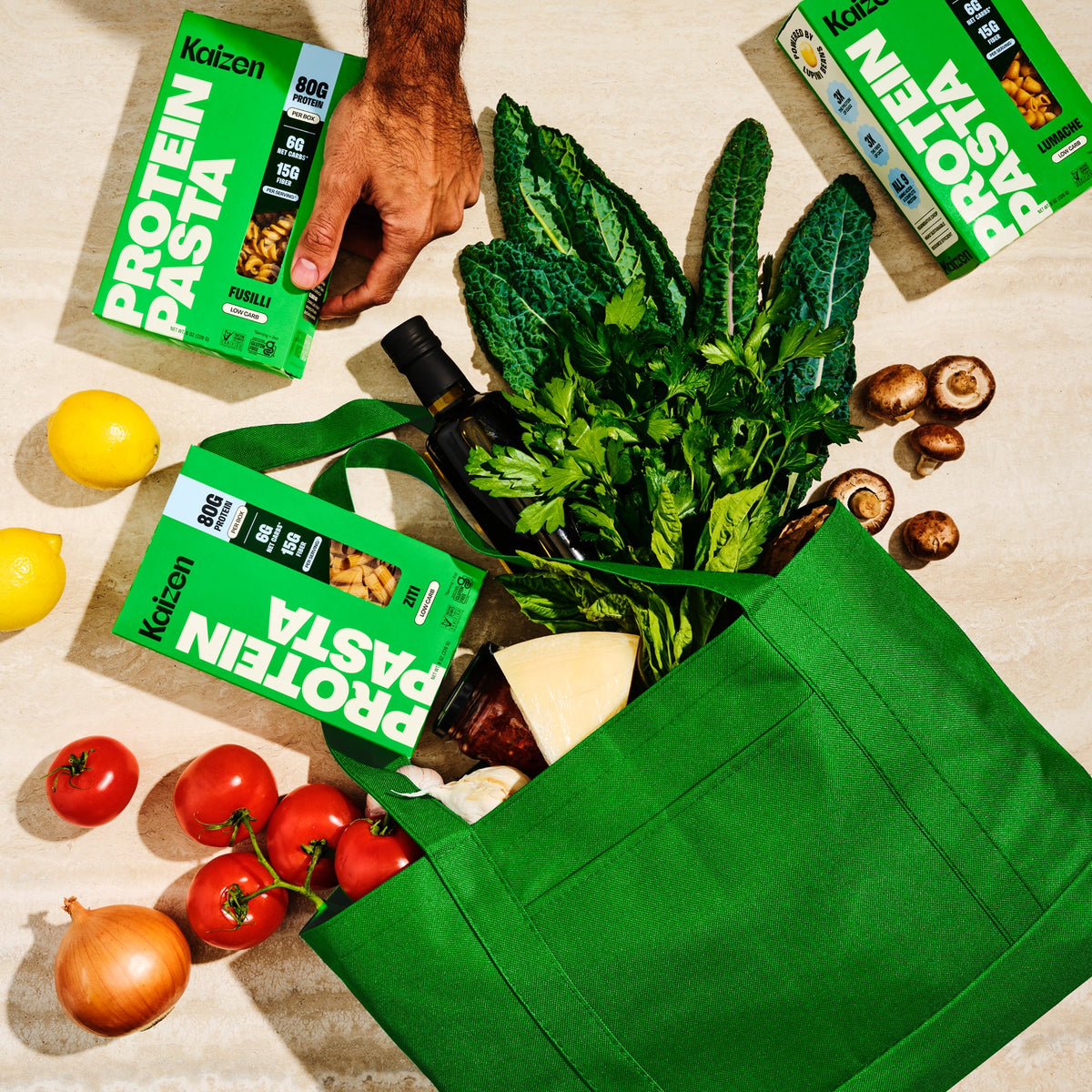 Kaizen Protein Pasta boxes in a green shopping bag with fresh vegetables