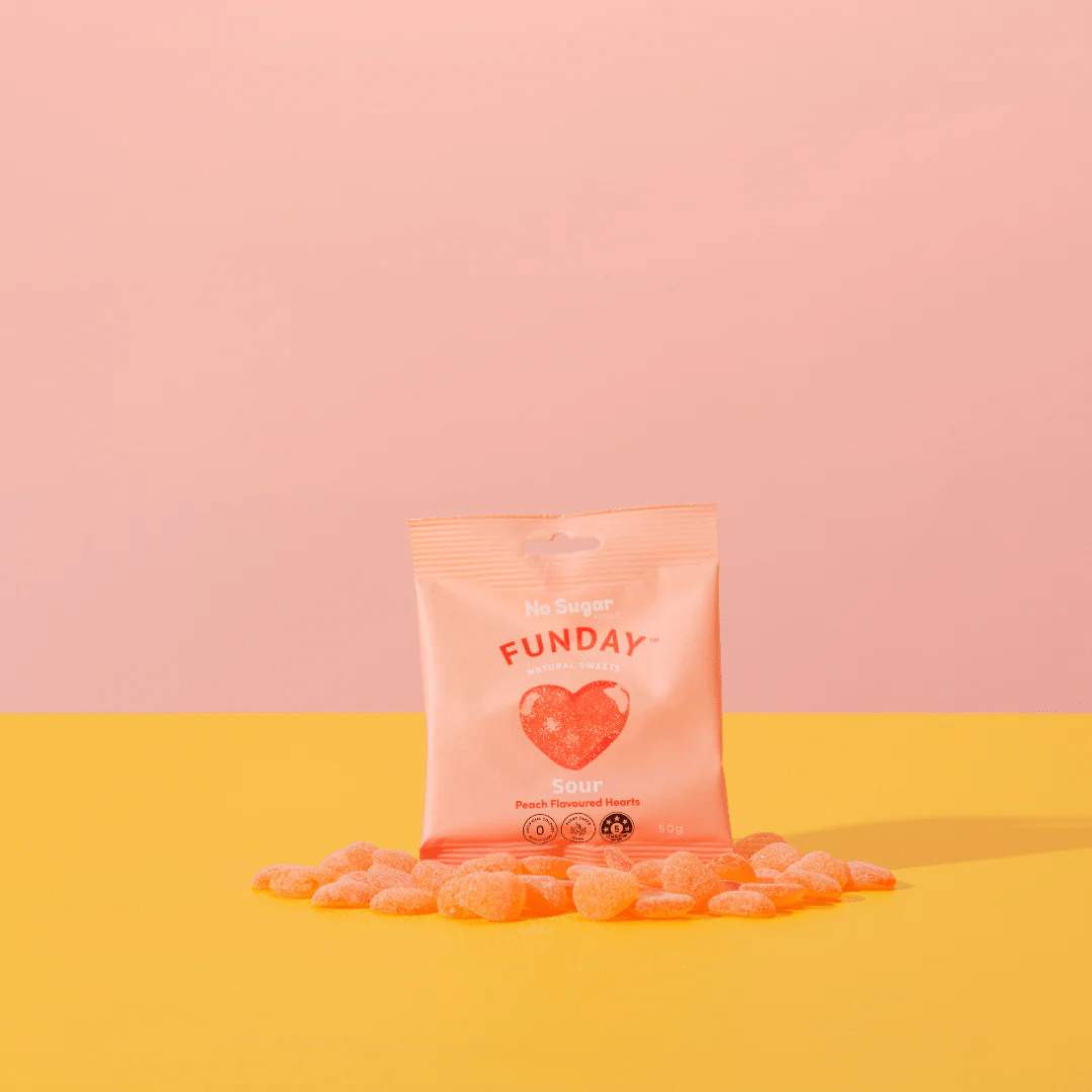Sour Peach Hearts - 50g x 12 by Funday in peach packaging with scattered sour peach heart gummies on yellow surface