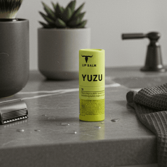 Yuzu Lip Balm - 7g by Bare Bones Beauty in bright yellow packaging on bathroom countertop with grooming items nearby